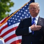 Donald Trump z ręką na sercu, na tle flagi Stanów Zjednoczonych