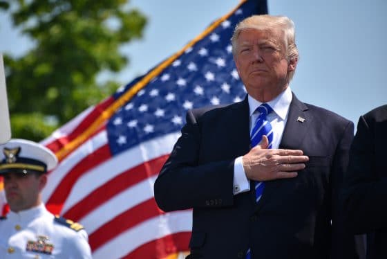Donald Trump z ręką na sercu, na tle flagi Stanów Zjednoczonych